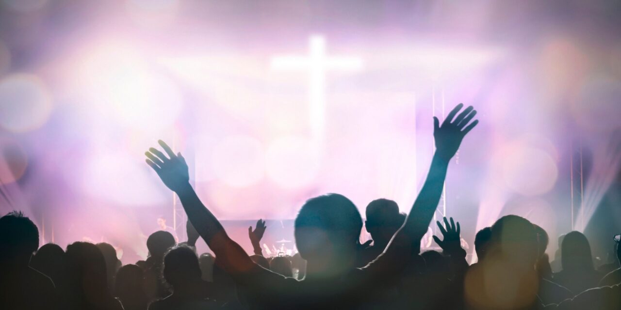 church congregation with arms up in worship with a cross